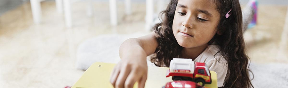 Tyttö leikkii keskittyneesti autoilla päiväkodissa.