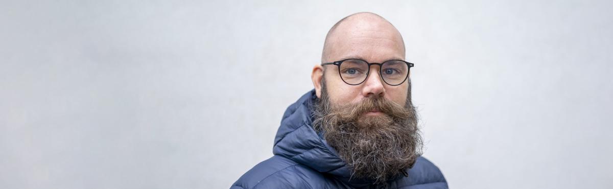 Parrakas mies katsoo kameraan.