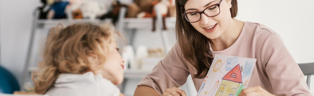 Silmälasipäinen nainen näyttää lapselle piirrosta.