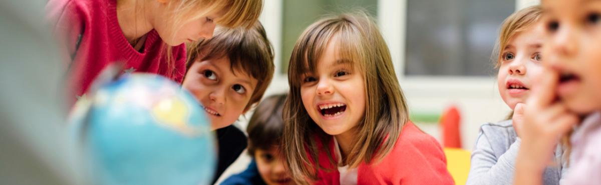 Kuusi esikouluikäistä lasta istuu pöydän ääressä. Etualalla näkyy karttapallo.