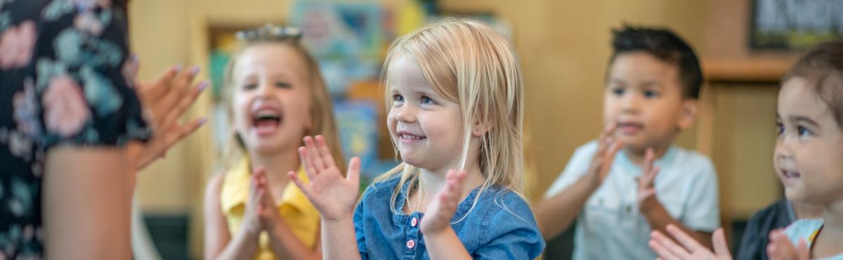 Päiväkoti-ikäiset lapset taputtavat keskittyneesti katse kiinnittyneenä aikuiseen, joka istuu heidän kanssaan lattialla.